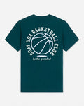 A dark teal green short-sleeve t-shirt with a white graphic print on the back featuring a basketball and the text 'GOAT USA BASKETBALL CLUB' and 'be the greatest'.