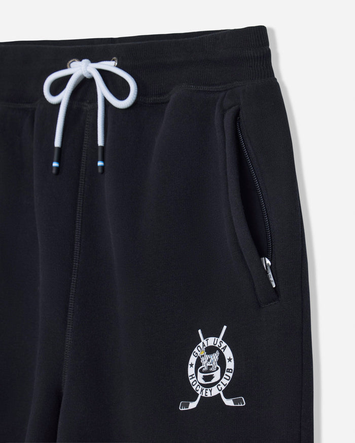 Close-up of black sweatpants with a white drawstring, side zip pocket, and a white hockey-themed crest logo near the lower left leg.
