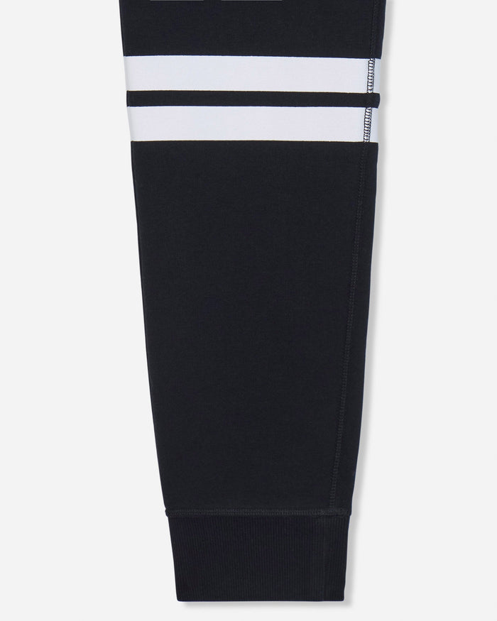 A close-up of a black garment leg with two horizontal white stripes near the upper section, shown against a light gray background.