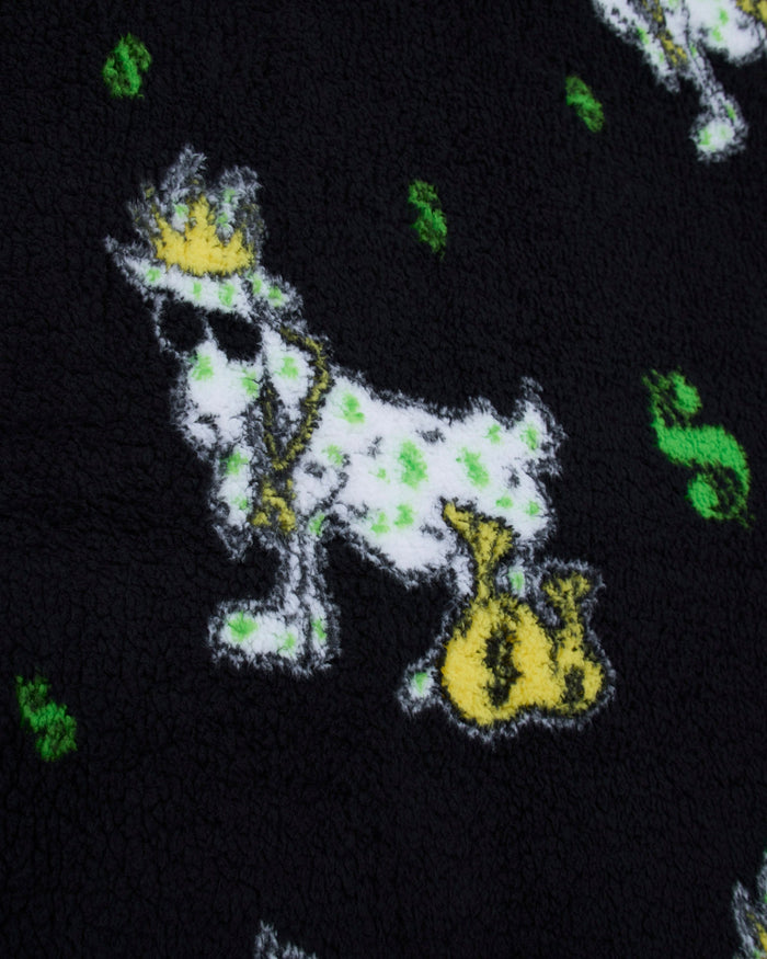 Close-up of a plush black fabric featuring a white goat wearing a gold crown and holding a gold money bag, with small green dollar-sign motifs scattered around.
