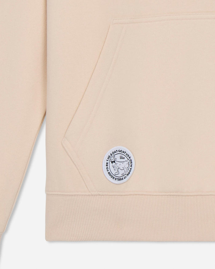 Beige sweatshirt with a logo patch on a light gray background