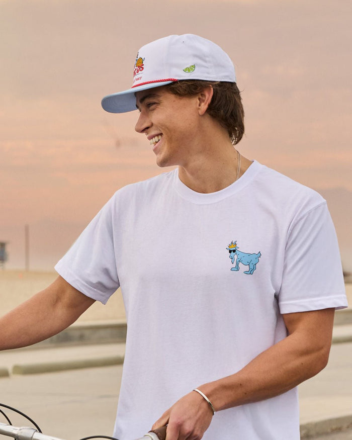 Person wearing a white t-shirt with a blue graphic and a white cap, standing outdoors.