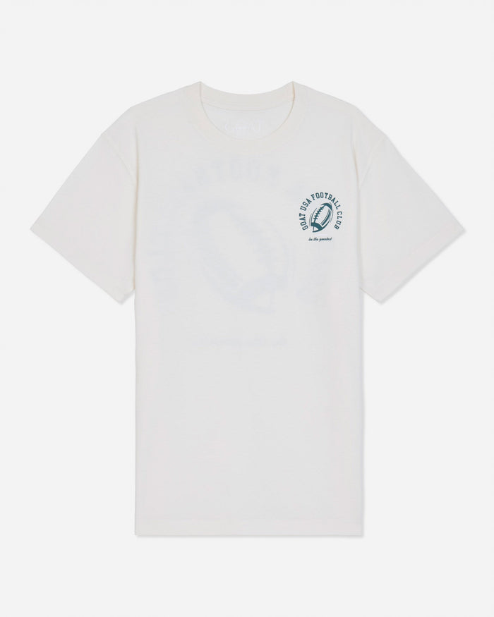 A white short-sleeve t-shirt with a small dark green circular graphic on the left chest featuring an football and the text 'GOAT USA FOOTBALL CLUB'.