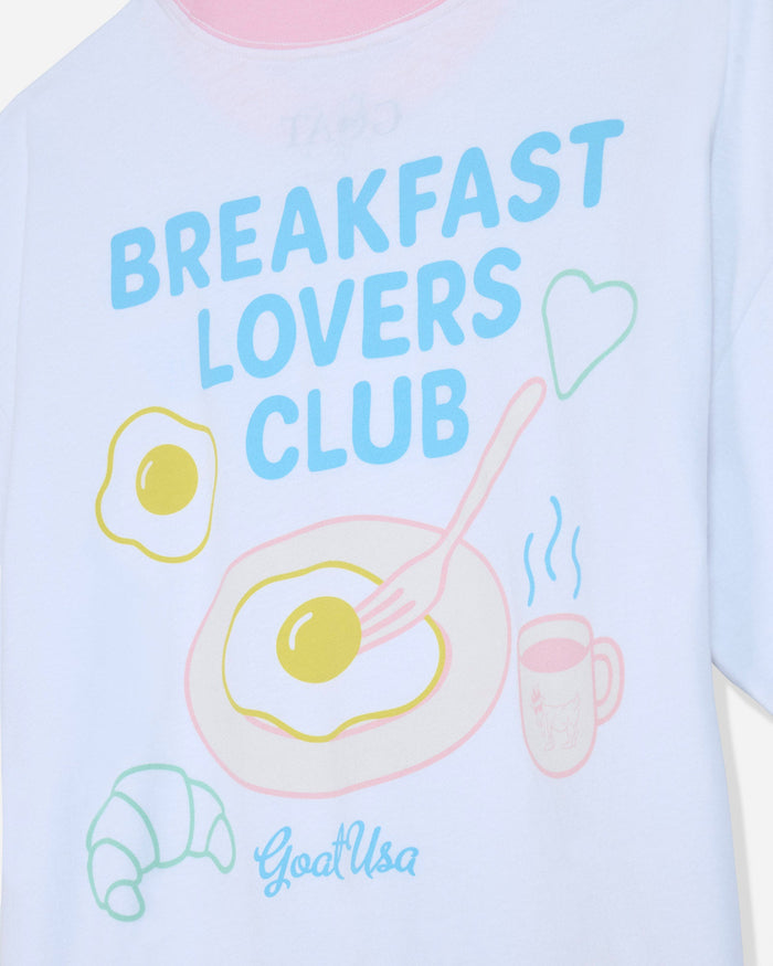 Close-up of white oversized t-shirt that says 'Breakfast Lovers Club' with various breakfast items