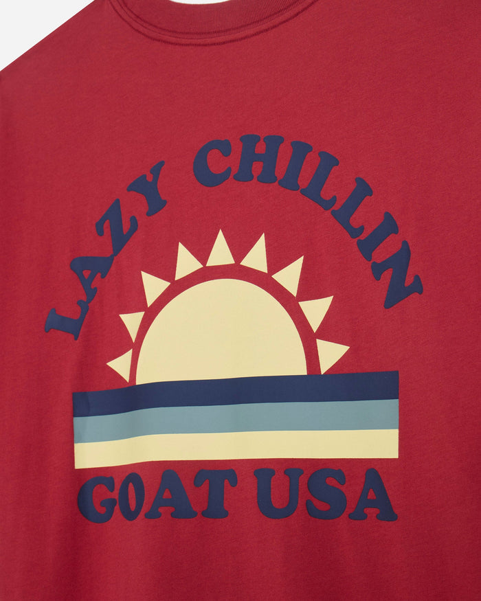 Close-up of red oversized t-shirt with sunset graphic and 'Lazy Chillin GOAT USA' text