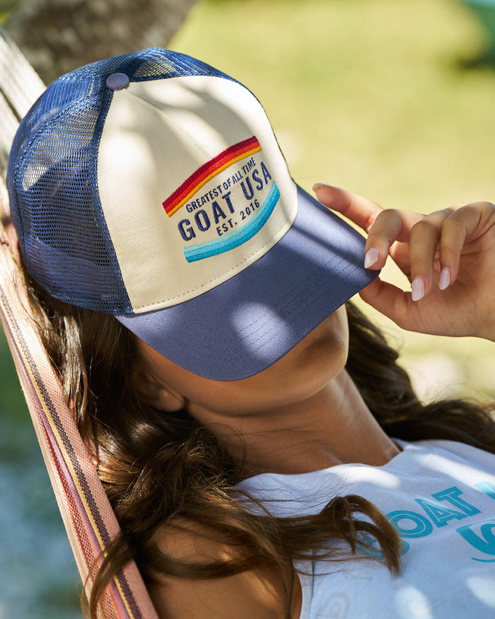 Girl laying on a hammock with a navy and cream hat covering her face