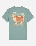 A sage green short-sleeve t-shirt with a retro graphic of a stack of pancakes wearing a crown and sunglasses, with the text 'HOT Goatcakes MADE FRESH' and 'GOAT USA BREAKFAST Union' on a light gray background.