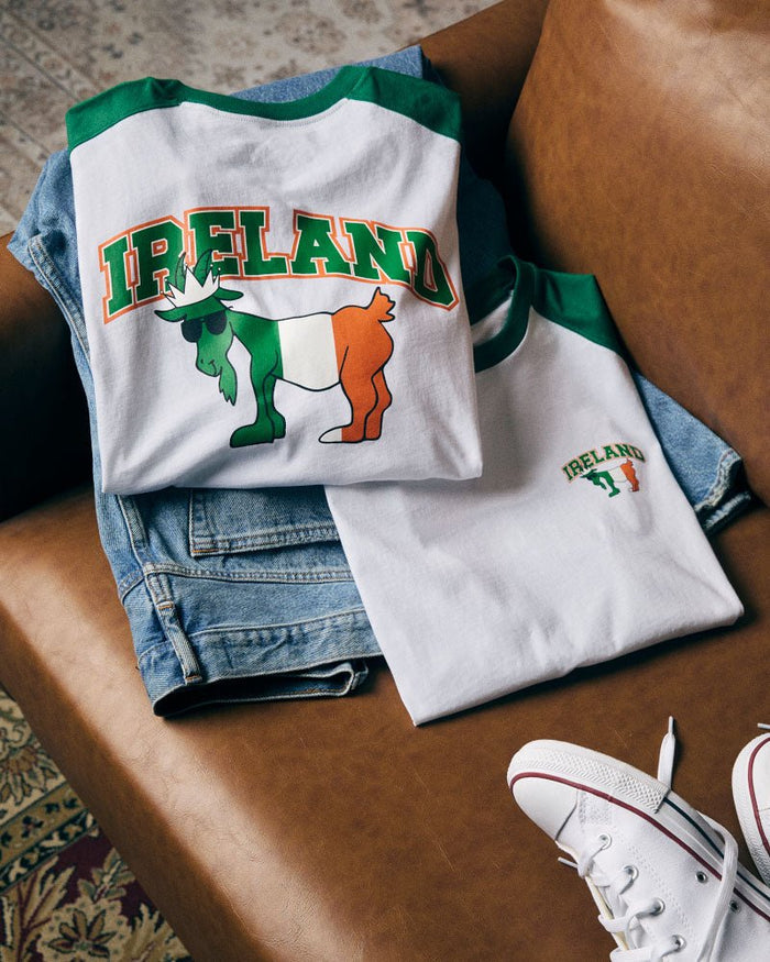 White t-shirt with 'IRELAND' and goat design on a brown surface with jeans and white sneakers.