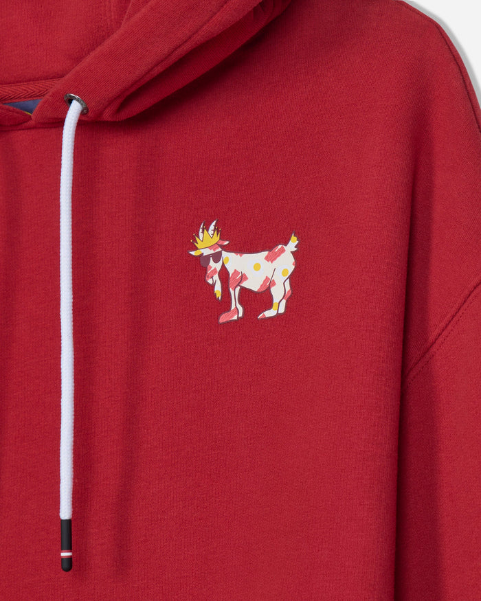 A close-up of a red hooded sweatshirt featuring a white drawstring and a small colorful embroidered goat character on the left chest.