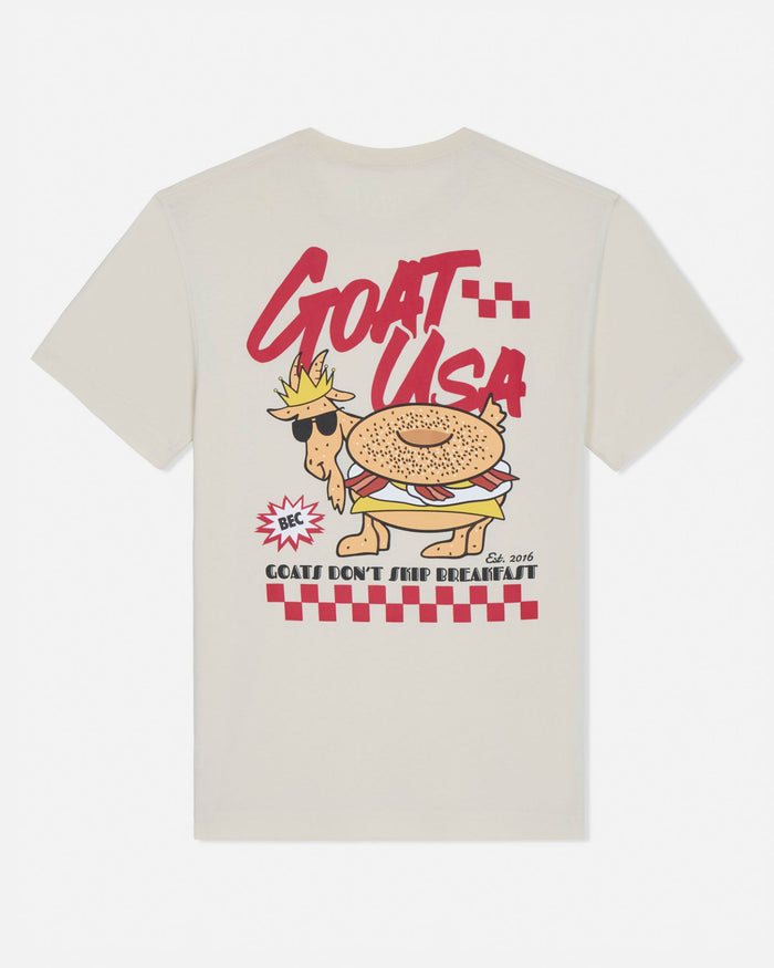 Beige t-shirt with a cartoon goat wearing sunglasses and a crown, labeled 'GOAT USA', on a white background.
