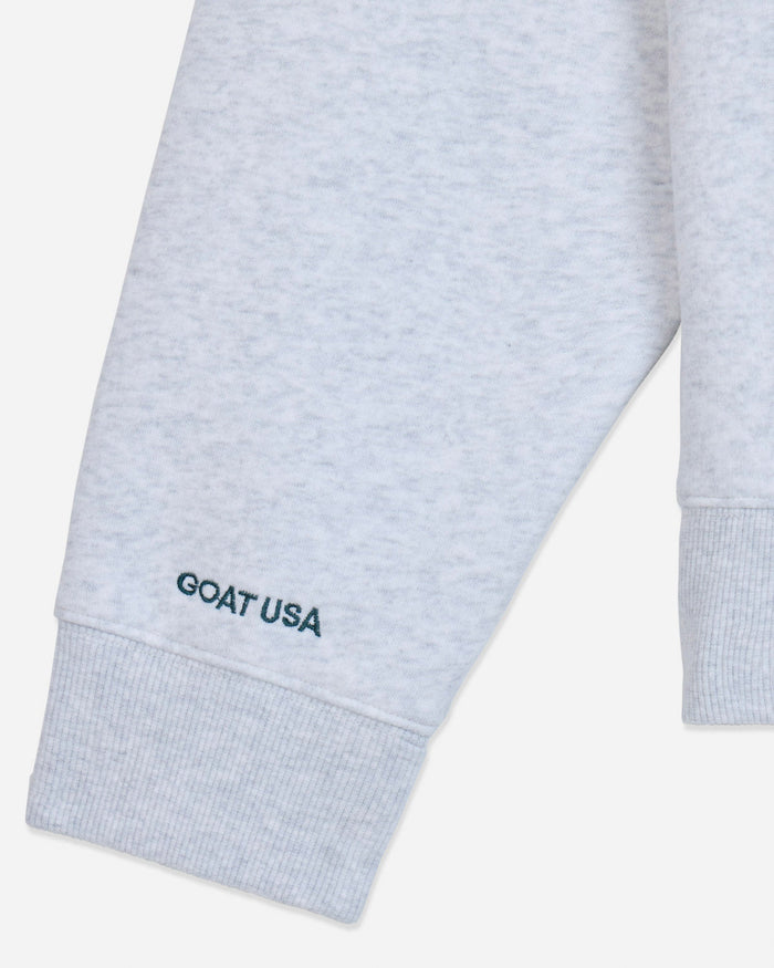 Close-up of a light heather gray sweatshirt sleeve with a ribbed cuff and the text 'GOAT USA' embroidered in dark teal near the hem.