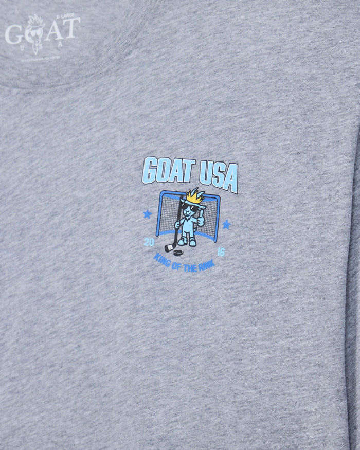 Close-up of a heather gray t-shirt featuring a 'GOAT USA' graphic on the chest with a cartoon hockey goat character and the text 'King of the Rink'.