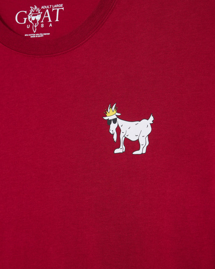 A close-up of a red t-shirt featuring a small white cartoon goat wearing a gold crown printed on the chest. The inside collar shows the 'GOAT USA' brand logo.#color_cranberry