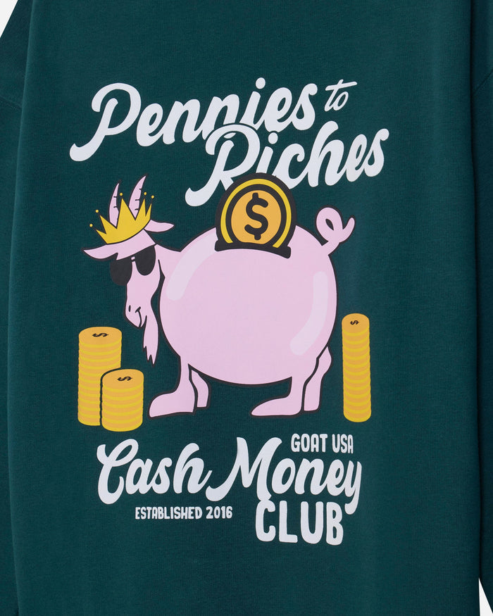 Close-up of a dark teal-green sweatshirt featuring a graphic print of a pink cartoon goat wearing a gold crown and sunglasses, surrounded by gold stacks of cash, with white and yellow text reading 'Pennies to Riches' and 'Cash Money CLUB'.