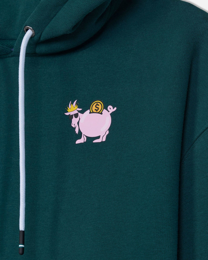 Close-up of a dark green hoodie featuring a small graphic of a pink goat carrying a gold coin on its back, with a white drawstring on the left side.