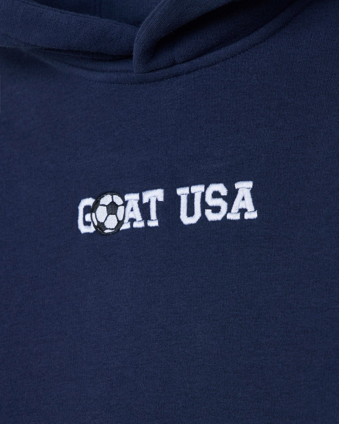 Close-up of a navy blue hoodie with 'GOAT USA' embroidered in white across the chest, where the letter O is replaced by a black-and-white soccer ball graphic.