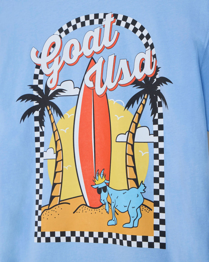 Light blue t-shirt with a graphic of a goat, surfboard, and palm trees on a checkered border.