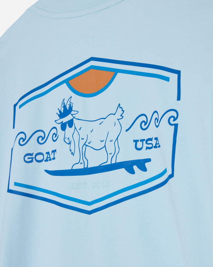 Light blue t-shirt with a graphic of a goat on a surfboard and 'GOAT USA' text, on a light blue background.#color_delicate-blue