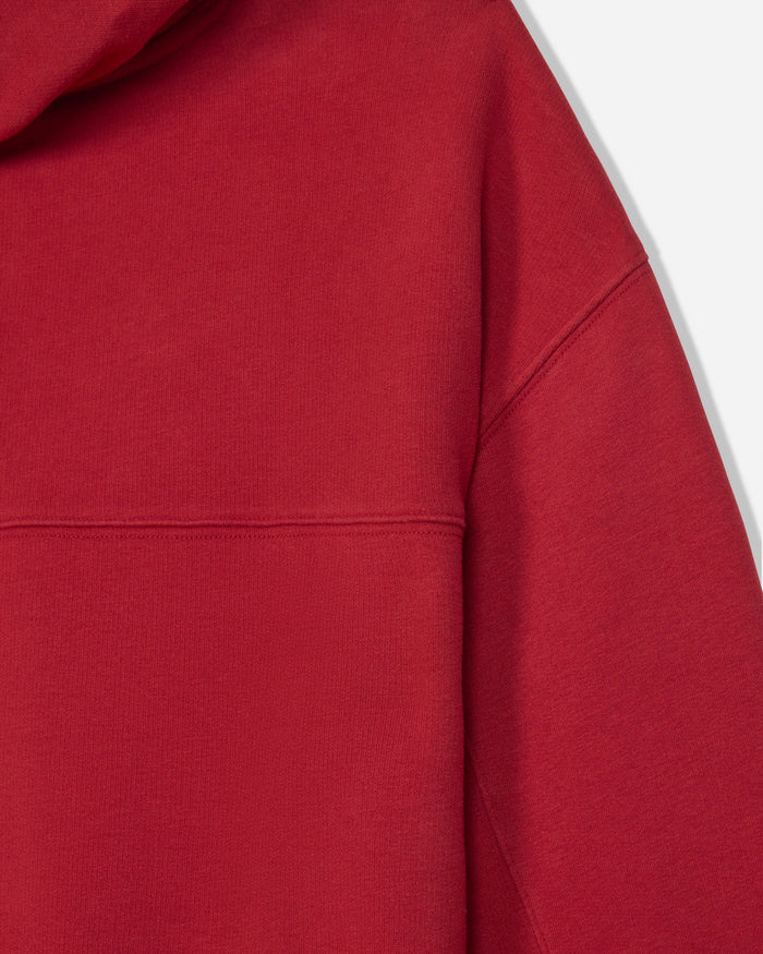 Close-up of a red hooded sweatshirt showing the fabric texture, hood edge, and shoulder seam against a light gray background.
