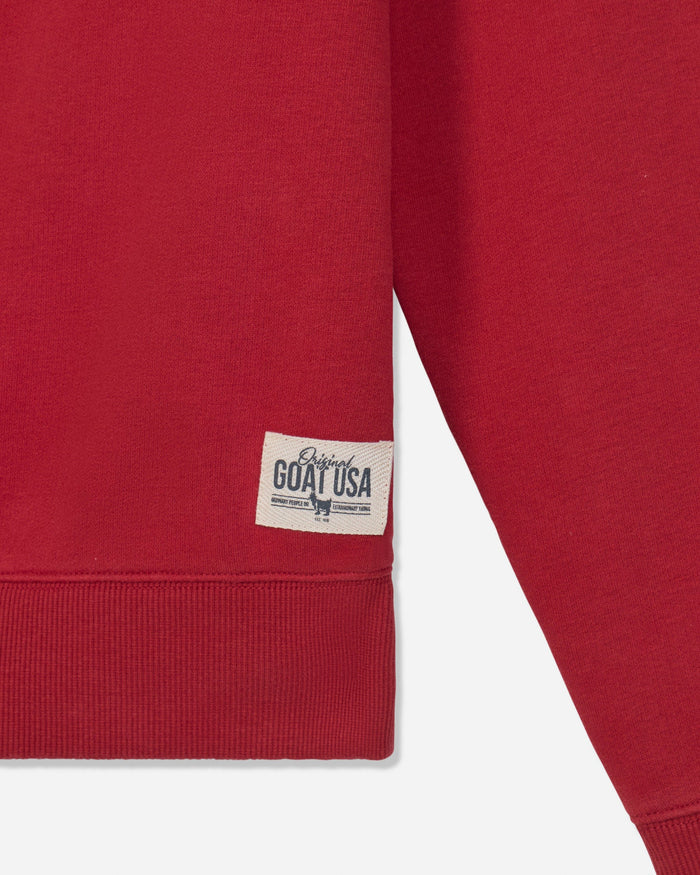 Close-up of a red sweatshirt sleeve and cuff with a small white woven label reading 'Original GOAT USA' on a light gray background.
