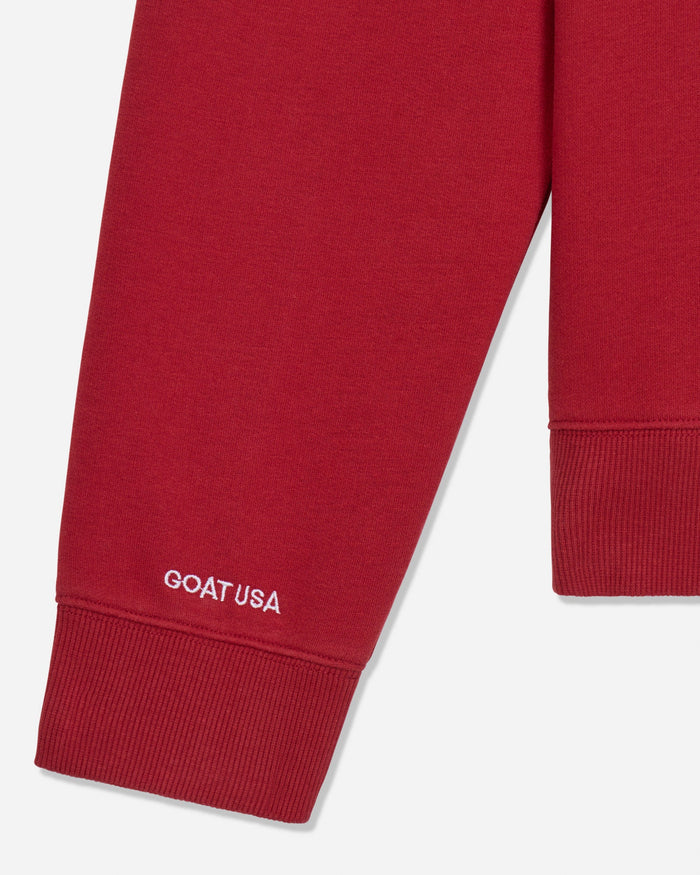 Close-up of a red ribbed sweatshirt sleeve with white GOAT USA text near the cuff, shown on a light gray background.