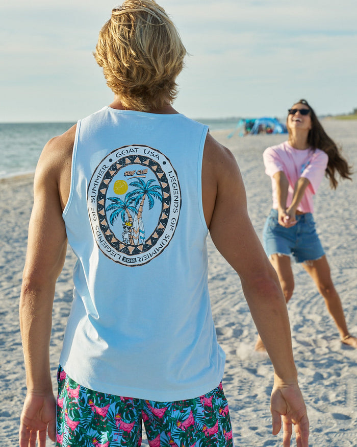 Guy wearing a blue tank top on a beach playing volleyball with a girl in a pink top