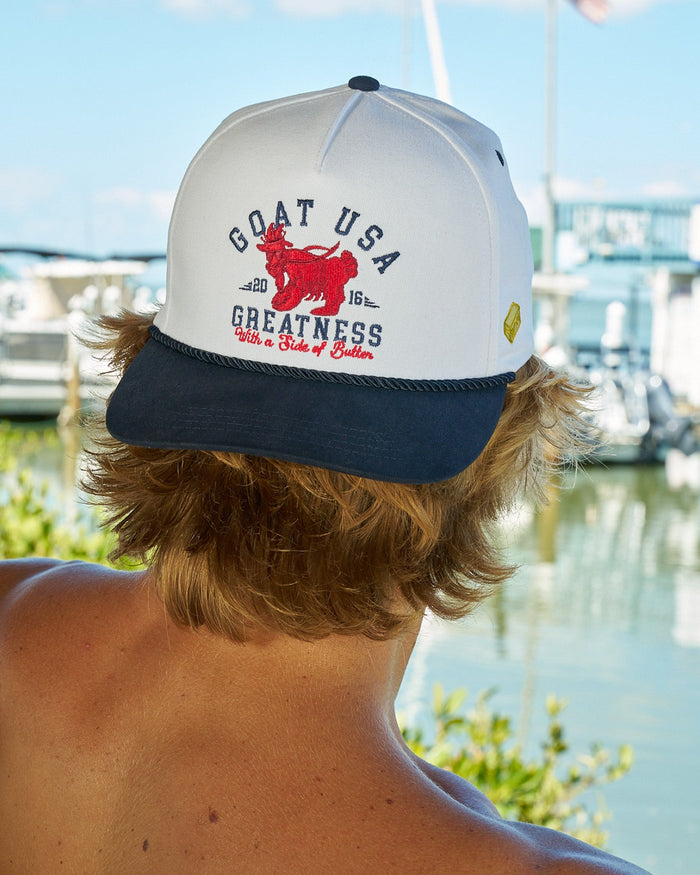 Man wearing backwards lobster hat with water and boats in the background