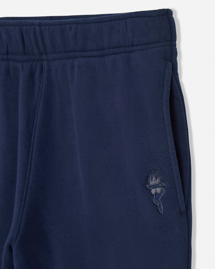 Close-up of navy blue sweatpants showing the elastic waistband, side pocket, and a small tonal embroidered logo on the thigh.#color_navy-blazer