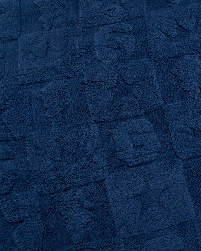 A close-up of a dark navy blue textured fabric with raised block patterns and tufted lettering.