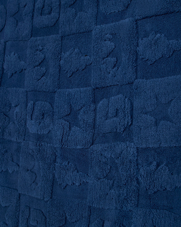 A close-up of a dark navy blue textured fabric with a repeating embossed block pattern.