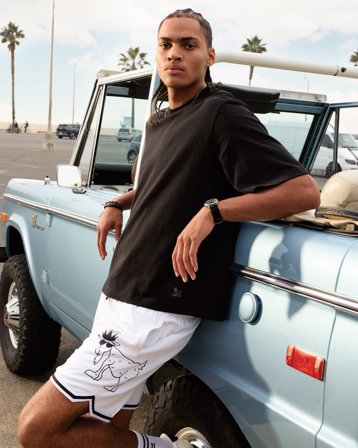 Person leaning against a vintage light blue truck with palm trees in the background#color_black