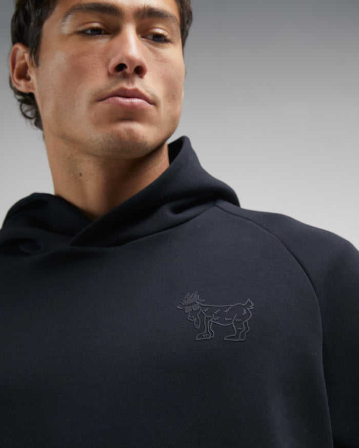 Man wearing a black hoodie with a logo on a gray background#color_black