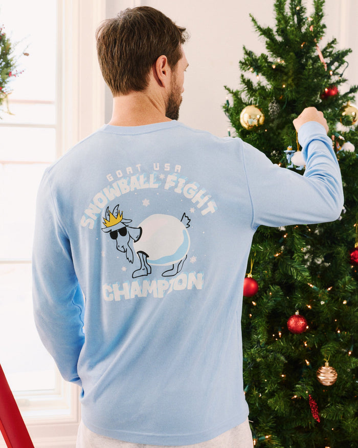 Man wearing a blue long-sleeve shirt with a graphic design in front of a decorated Christmas tree.
