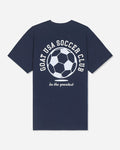 A navy blue short-sleeve t-shirt with a white graphic on the back featuring a soccer ball and the text 'GOAT USA SOCCER CLUB' and 'be the greatest'.