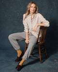 A person sits on a wooden chair against a dark backdrop, wearing a striped shirt, yellow socks, burgundy loafers, and The Fleece Stadium Sweatpant in Dark Heather Grey by THE GREAT. F26 D1 FLEECE BACK KNITS.