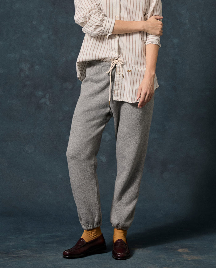 A person stands with arms folded, wearing a striped shirt, The Fleece Stadium Sweatpant in Dark Heather Grey by THE GREAT. F26 D1 FLEECE BACK KNITS, mustard socks, and dark brown loafers against a dark blue mottled background.
