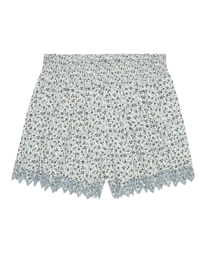 The Smocked Eyelet Short in Bluebell Ditsy by The Great. SP26 Sleep features a light blue smocked design, elastic waistband, and scalloped embroidered eyelet trim at the hem, shown against a white background.