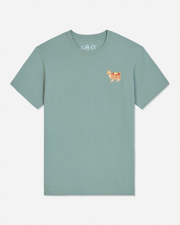 A sage green short-sleeve t-shirt featuring a small embroidered goat logo on the left chest in orange and white.