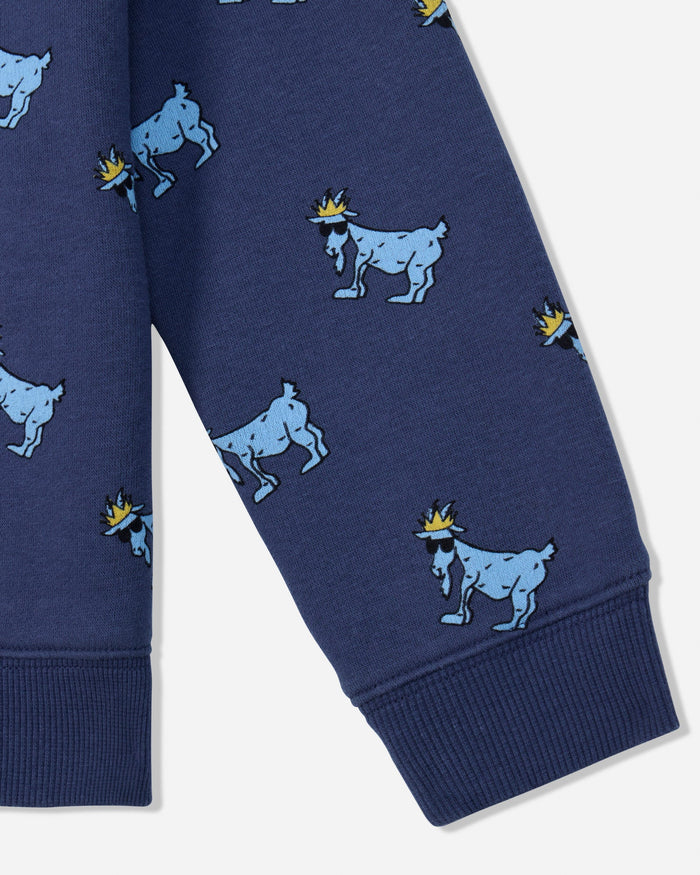 Close-up of a navy blue garment, likely a sweatshirt or pants leg, featuring an allover print of light blue goats wearing small yellow crowns, with ribbed cuffs at the bottom.#color_navy