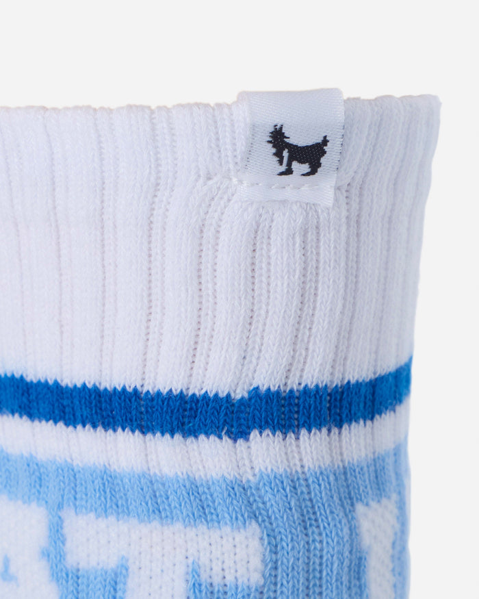 Close-up of a white ribbed knit sock with a blue horizontal stripe and a small black goat logo on a white fabric tag near the cuff.