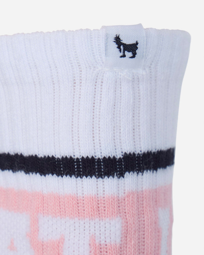 Close-up of a white ribbed knit sock with a black horizontal stripe and a pink graphic pattern at the bottom, featuring a small black goat logo on a white tag at the cuff.#color_pink