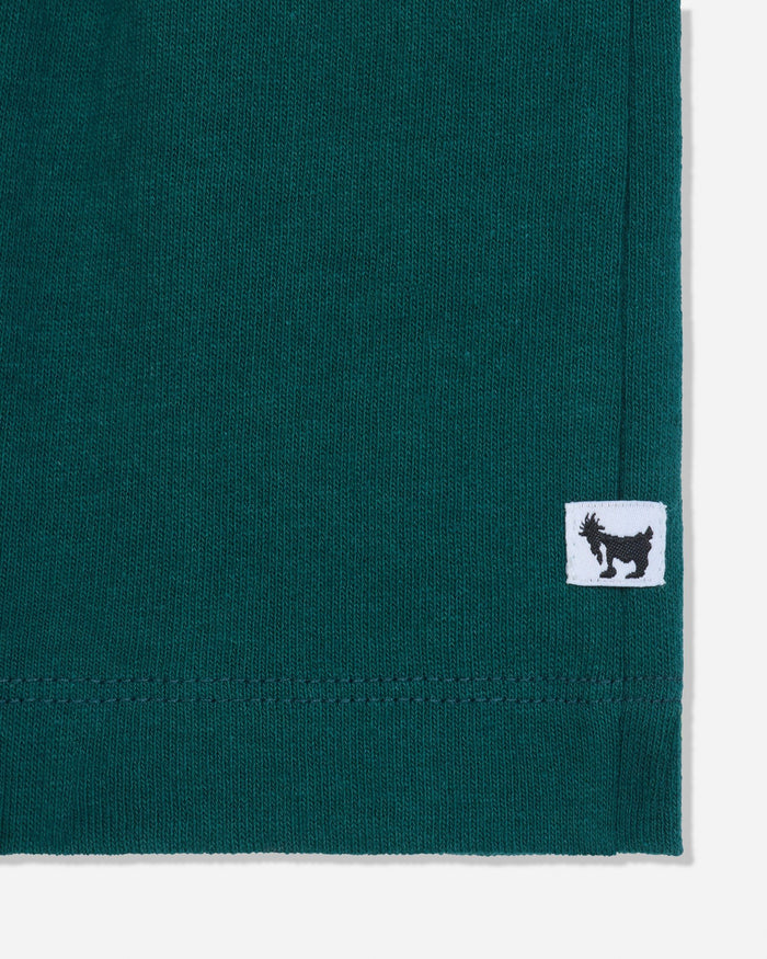 Close-up of a dark teal green knit fabric corner with a small white square patch featuring a black goat logo.